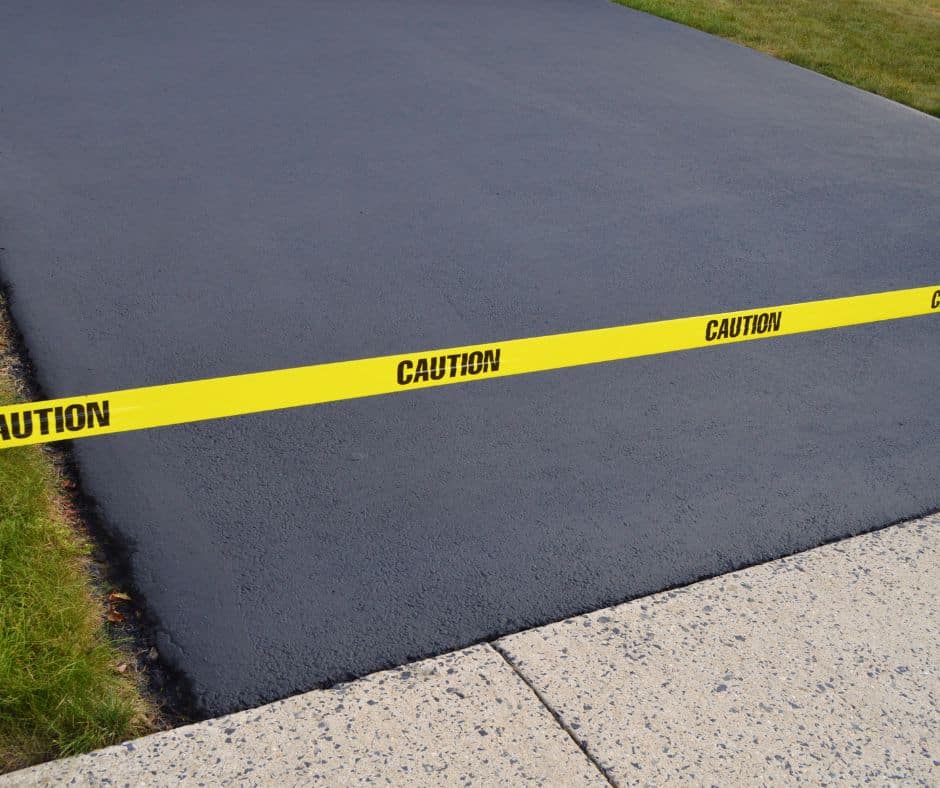 Freshly asphalted surface sectioned off with yellow caution tape against a sidewalk.