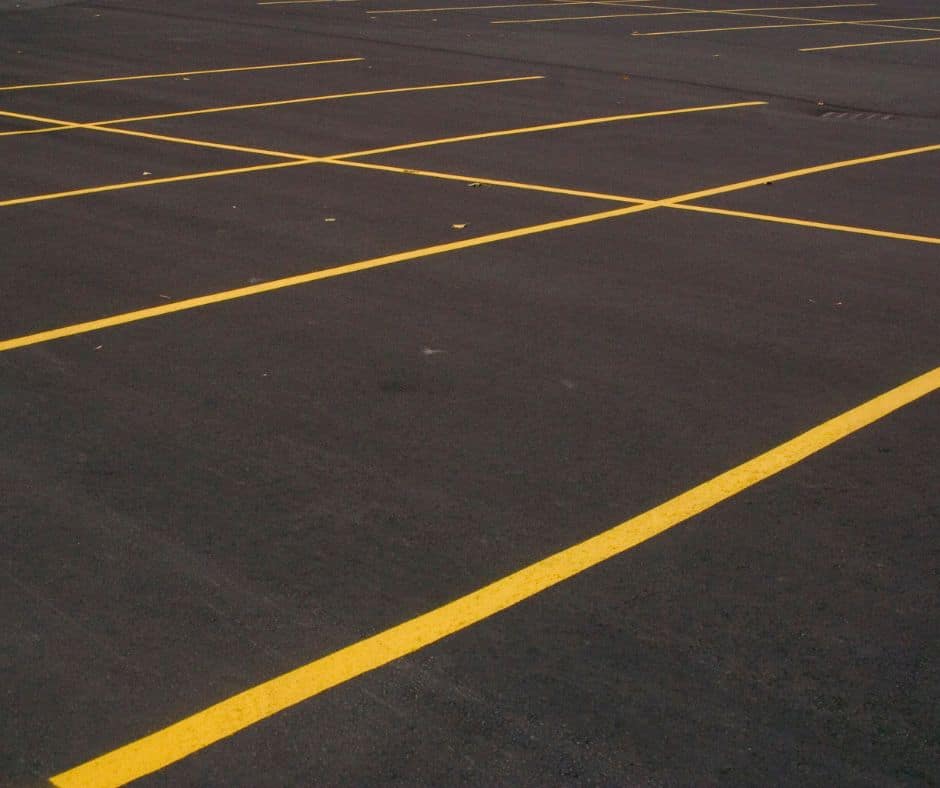 Dark asphalt parking lot with bright yellow parking bay lines, empty and clean.
