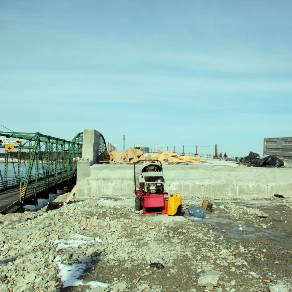 Construction site with concrete foundations, a generator, and rubble in the foreground, steel reinforcements, and clear sky.