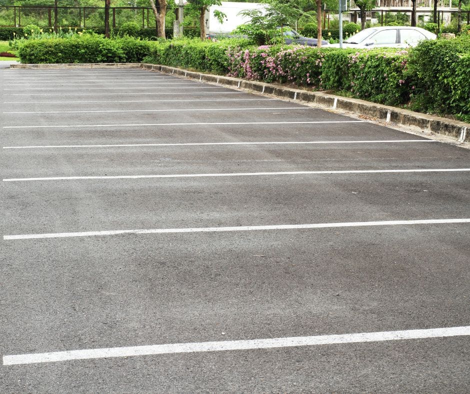 Spacious outdoor parking lot with white parking lines, surrounded by lush green hedges and flowering shrubs.