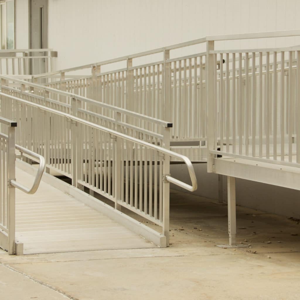 Accessible ramp with white metal railings leading to a building, ensuring facility entry for individuals with disabilities or mobility issues.