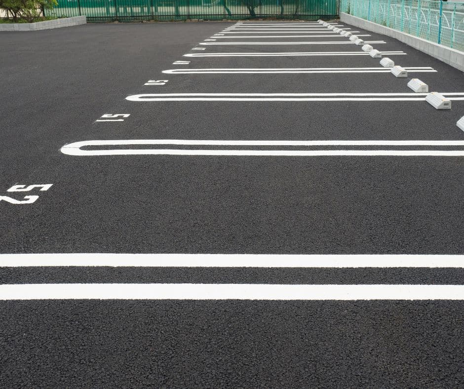New asphalt parking lot with freshly painted white parking space lines and numbered stalls.