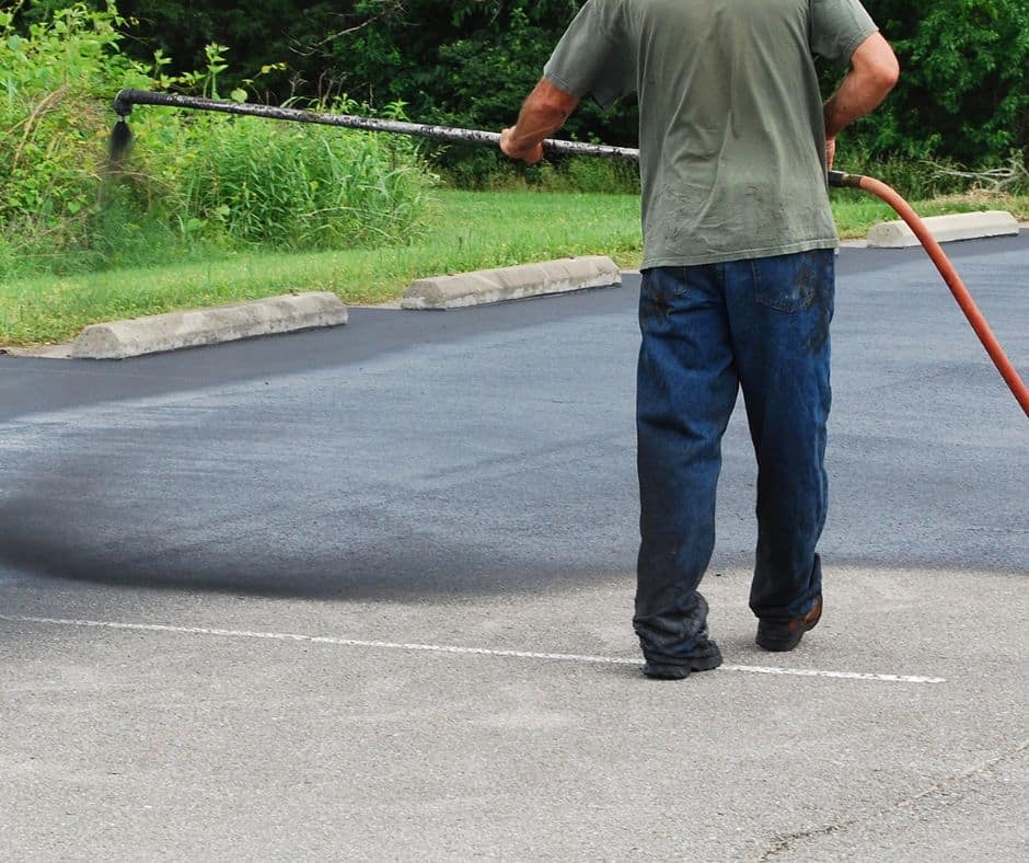 Worker applying sealant to a freshly asphalted parking lot with a long-handled applicator.