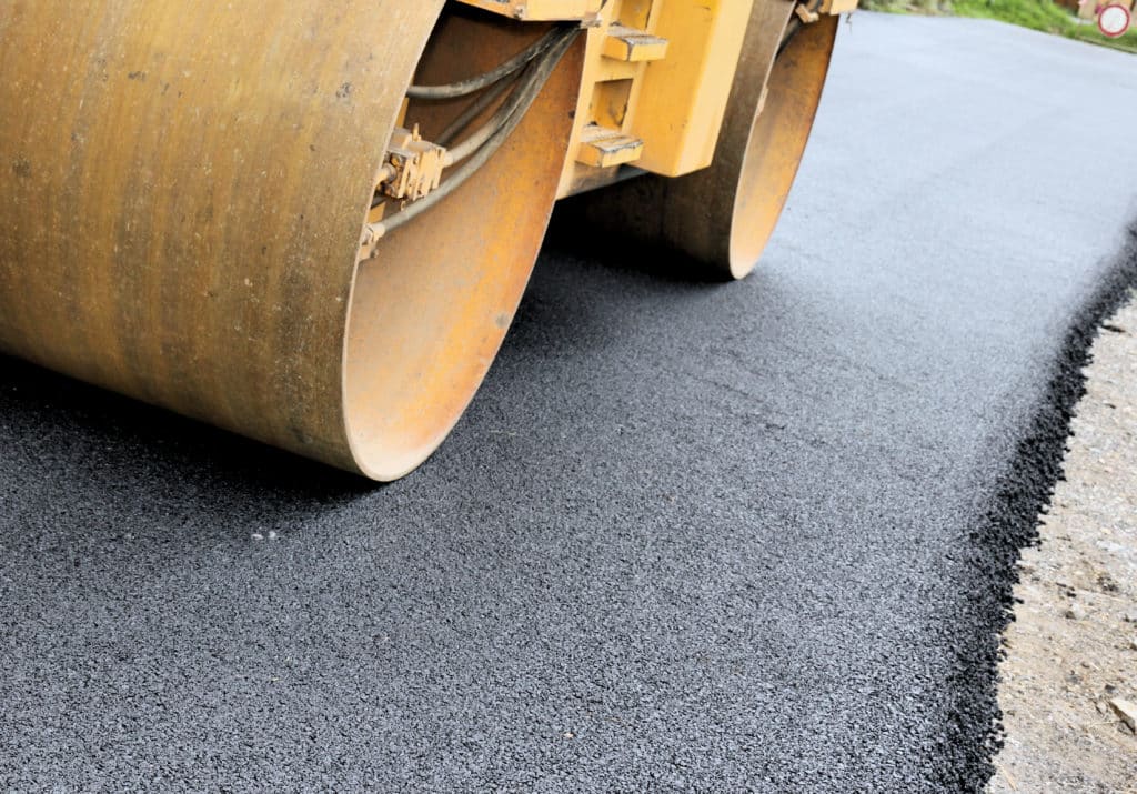 Yellow steamroller compacting freshly laid blacktop asphalt on a road construction site.