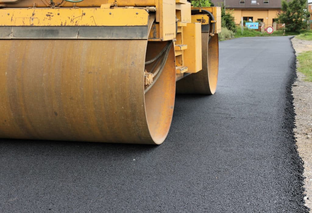 Close-up of the large steel rollers of a yellow steamroller on new asphalt pavement.