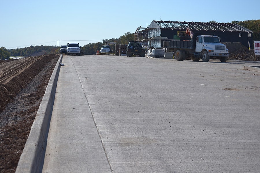 Fresh concrete roadway with curb and construction vehicles in the background on a clear day at a construction site.