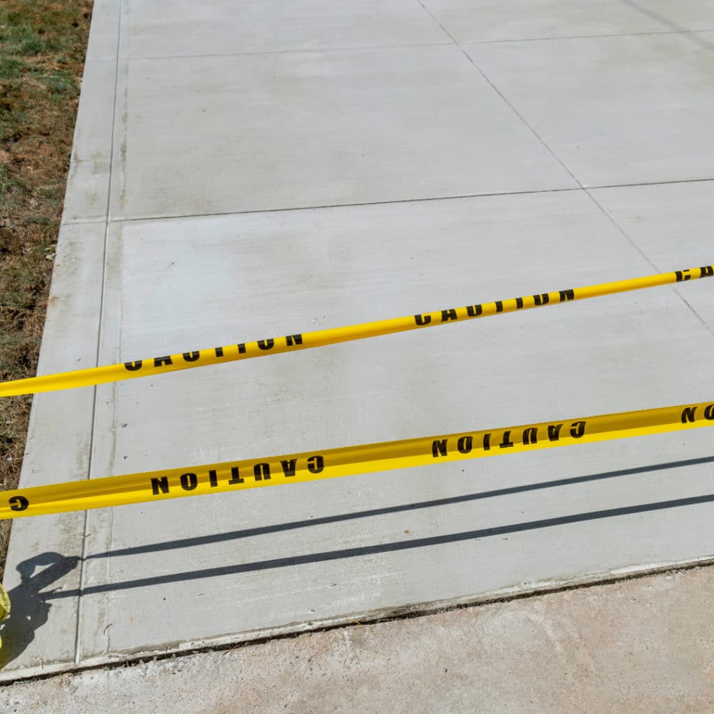 Fresh concrete sidewalk sectioned off by yellow caution tape with the word 'CAUTION' repeated across it.