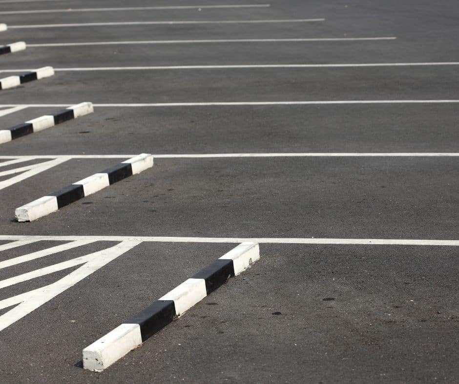 Empty parking lot with diagonal white lines and concrete wheel stops under bright sunlight.